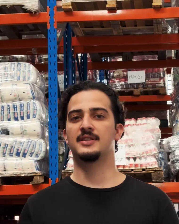 Gabriel Medeiros, um dos fundadores da Ufoody, num galpão de distribuidora, diante das prateleiras de paletes.
